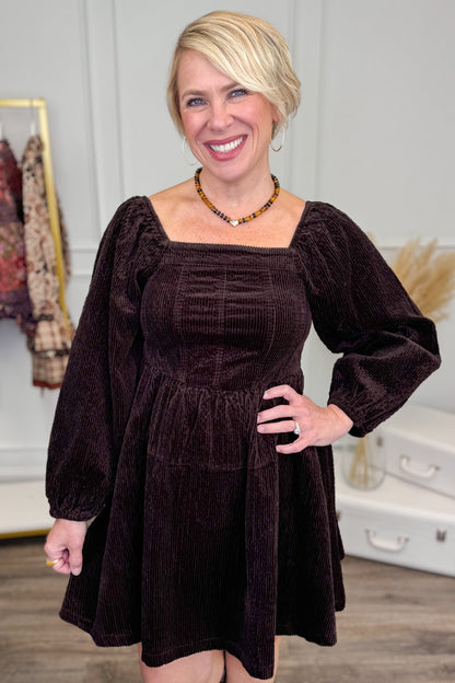 Woman wearing Brown Corduroy Puff Sleeve Dress and boots with decor in background.