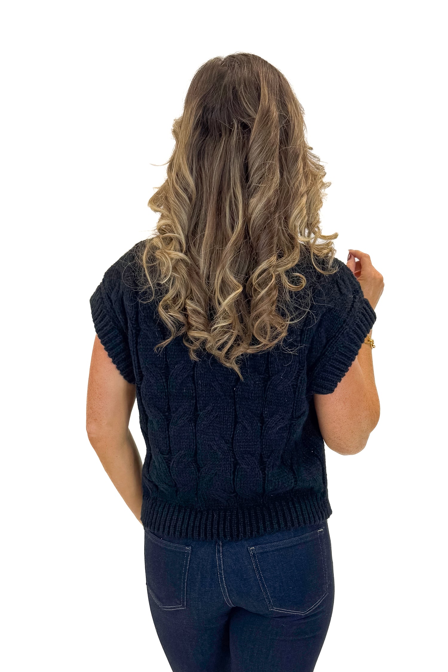 Back view of woman wearing Black Cable Knit Short Sleeve Sweater with jeans against white studio background.