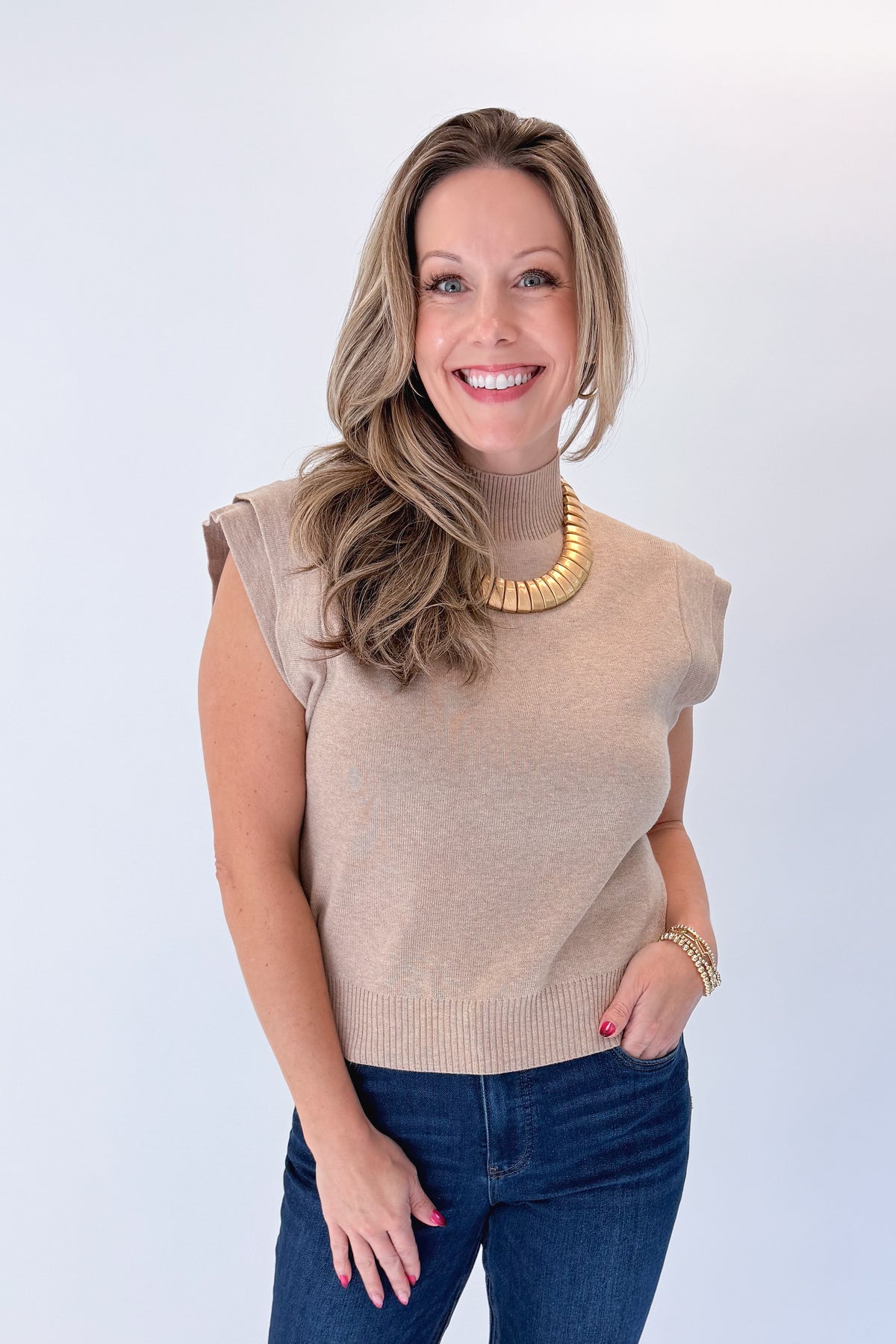 Front view of woman wearing Swagger Boutique’s Oatmeal Mock Neck Sleeveless Sweater by Entro with jeans against white studio background.