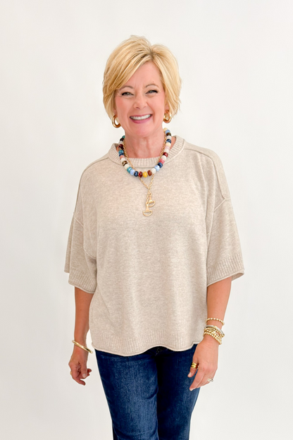 Front view of woman wearing Swagger Boutique’s Oatmeal Short Sleeve Sweater with jeans against white studio background.