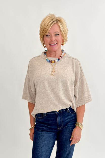 Front view of woman wearing Swagger Boutique’s Oatmeal Short Sleeve Sweater with jeans against white studio background.