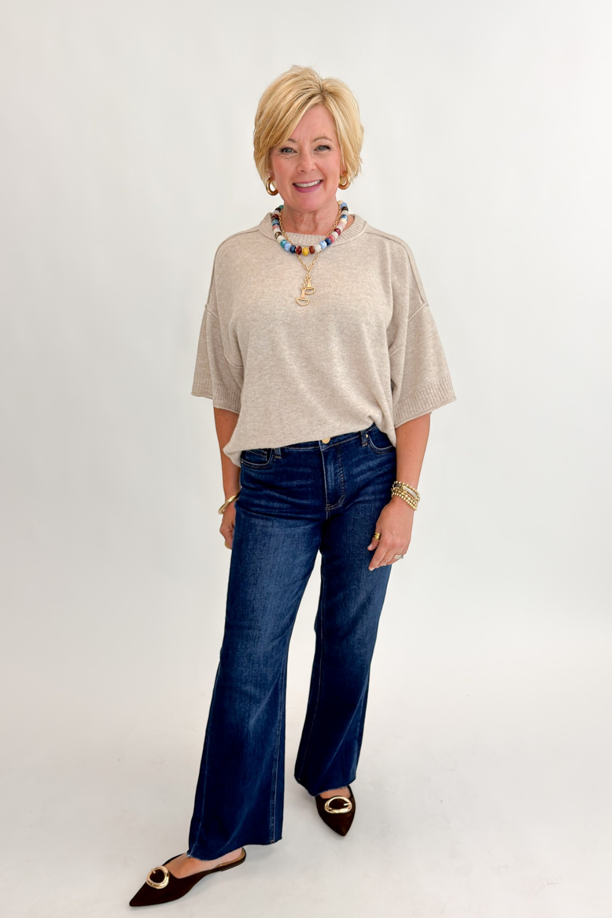 Front view of woman wearing Swagger Boutique’s Oatmeal Short Sleeve Sweater with jeans against white studio background.