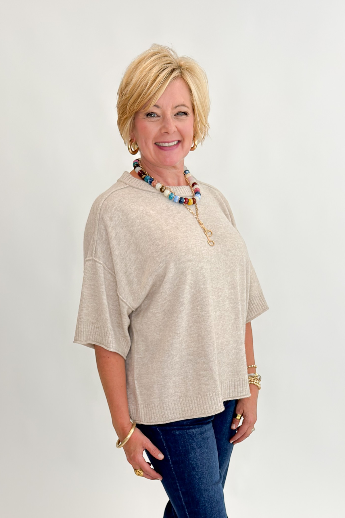 Side view of woman wearing Swagger Boutique’s Oatmeal Short Sleeve Sweater with jeans against white studio background.