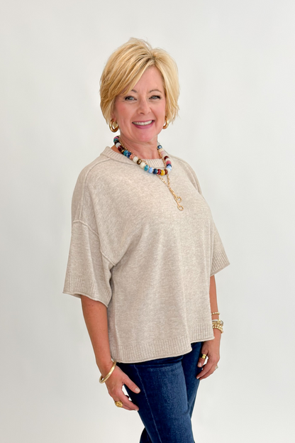 Side view of woman wearing Swagger Boutique’s Oatmeal Short Sleeve Sweater with jeans against white studio background.