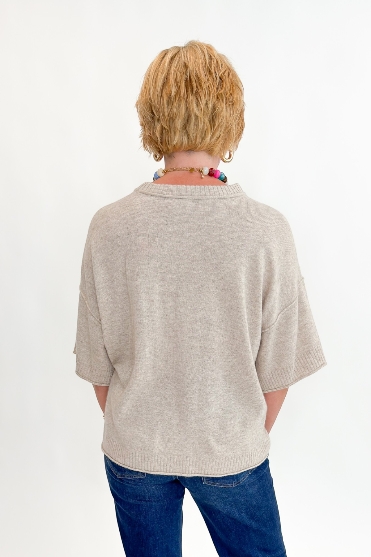Back view of woman wearing Swagger Boutique’s Oatmeal Short Sleeve Sweater with jeans against white studio background.