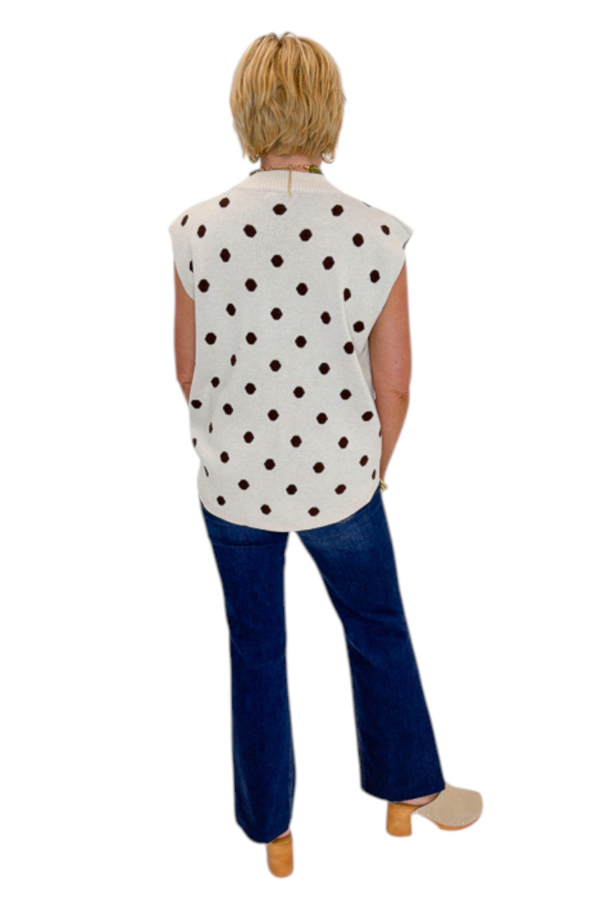 Back view of woman wearing Swagger Boutique’s Oatmeal &amp; Brown Polka Dot Sleeveless Sweater by Entro with jeans against white studio background.