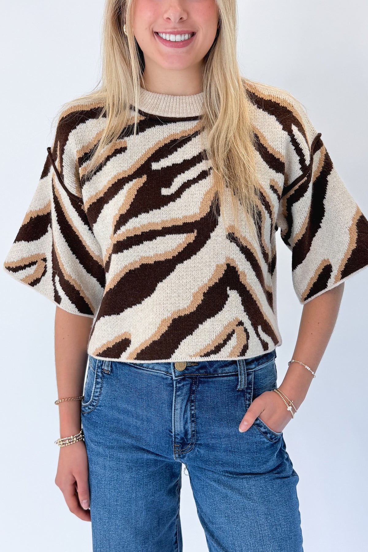 Front detail view of woman wearing Swagger Boutique’s Oatmeal &amp; Brown Zebra Short Sleeve Sweater by Entro with jeans against white studio background.