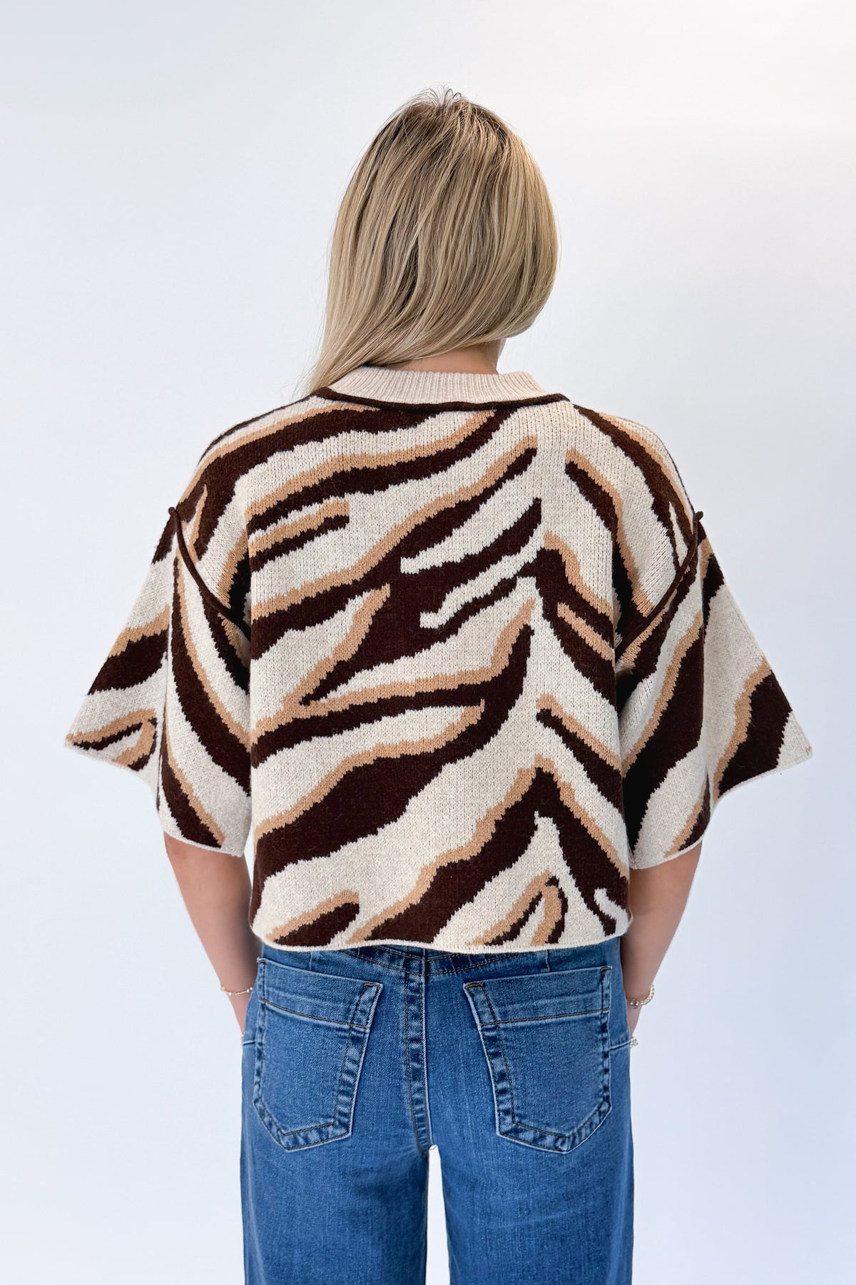 Back view of woman wearing Swagger Boutique’s Oatmeal &amp; Brown Zebra Short Sleeve Sweater by Entro with jeans against white studio background.