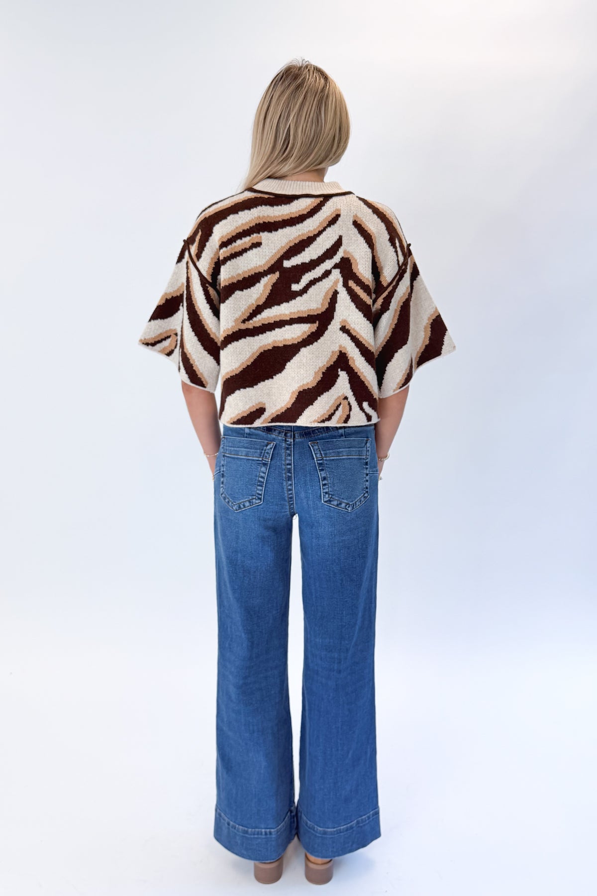Back view of woman wearing Swagger Boutique’s Oatmeal &amp; Brown Zebra Short Sleeve Sweater by Entro with jeans against white studio background.