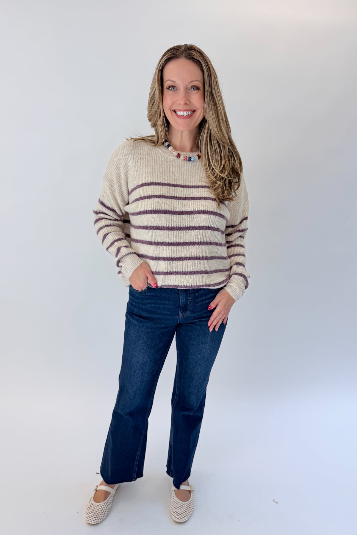 Front view of woman wearing Swagger Boutique’s Oatmeal &amp; Purple Striped Sweater with jeans against white studio background.