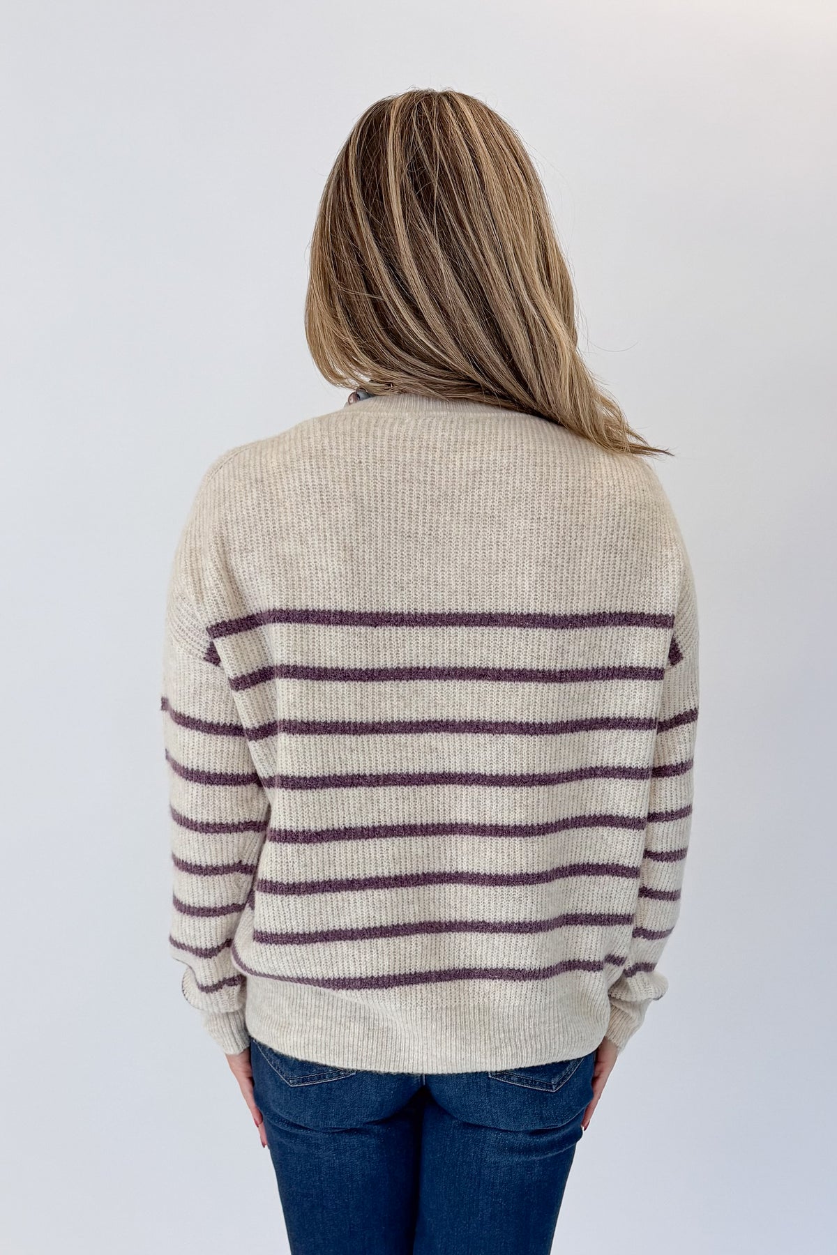 Back view of woman wearing Swagger Boutique’s Oatmeal &amp; Purple Striped Sweater with jeans against white studio background.
