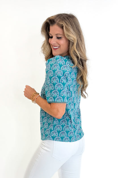 Side view of woman wearing Swagger Boutique’s Ocean Sunshower Flora Adelyn Top by Mary Square with jeans against white studio background.