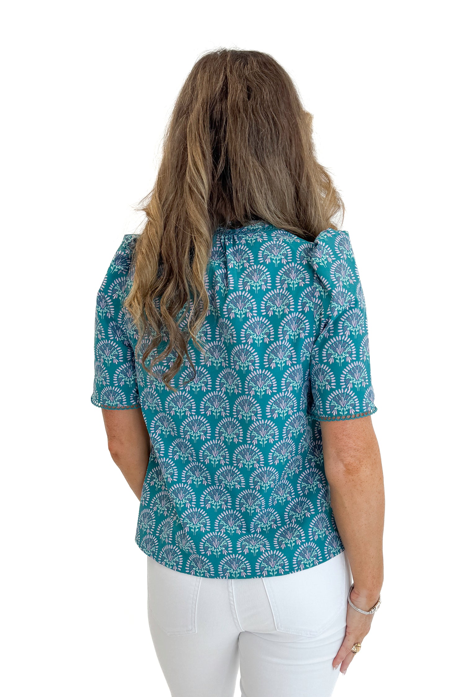 Back view of woman wearing Swagger Boutique’s Ocean Sunshower Flora Adelyn Top by Mary Square with jeans against white studio background.