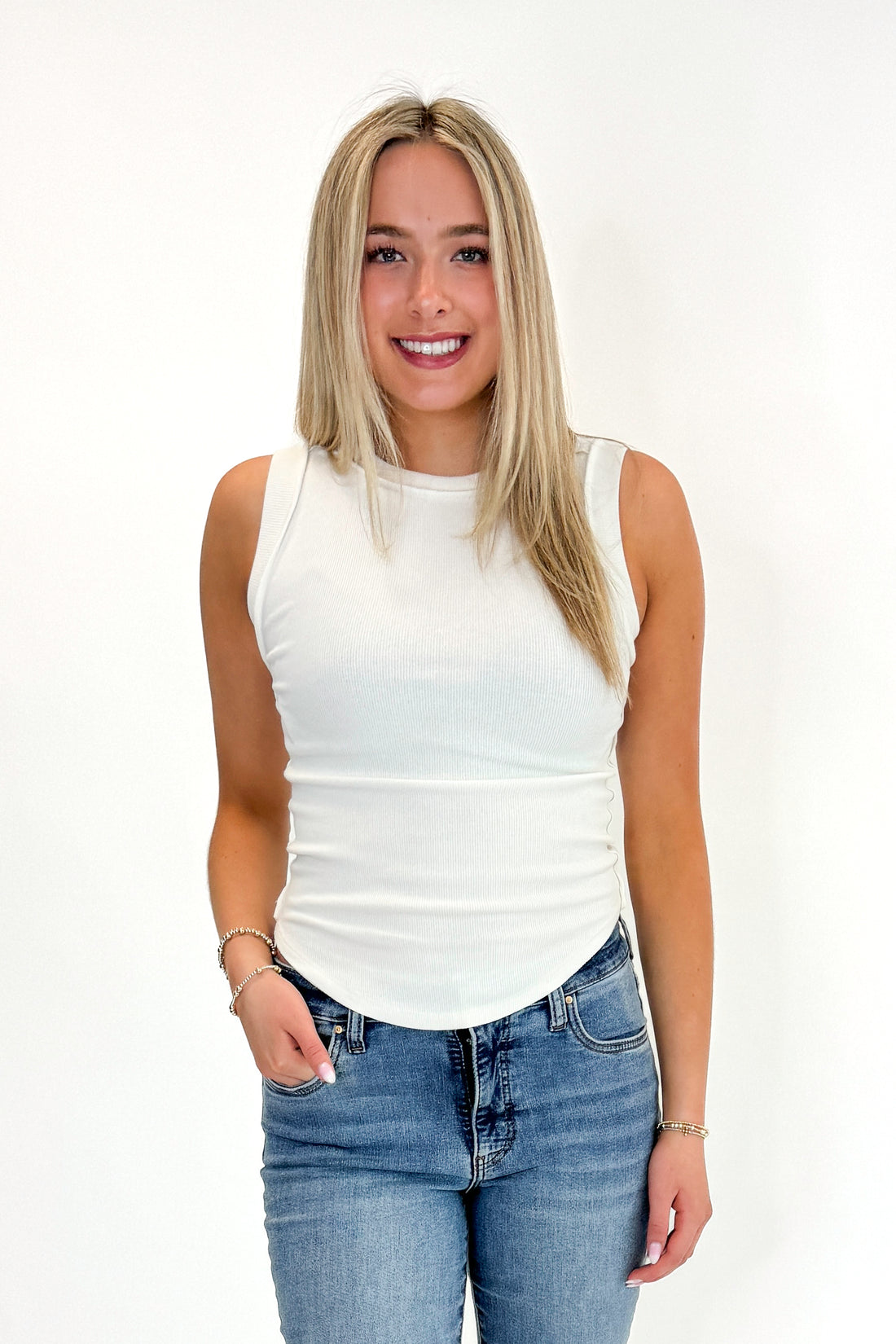 Front view of woman wearing Swagger  Off White Round Hem Ribbed Tank with jeans against white studio background.
