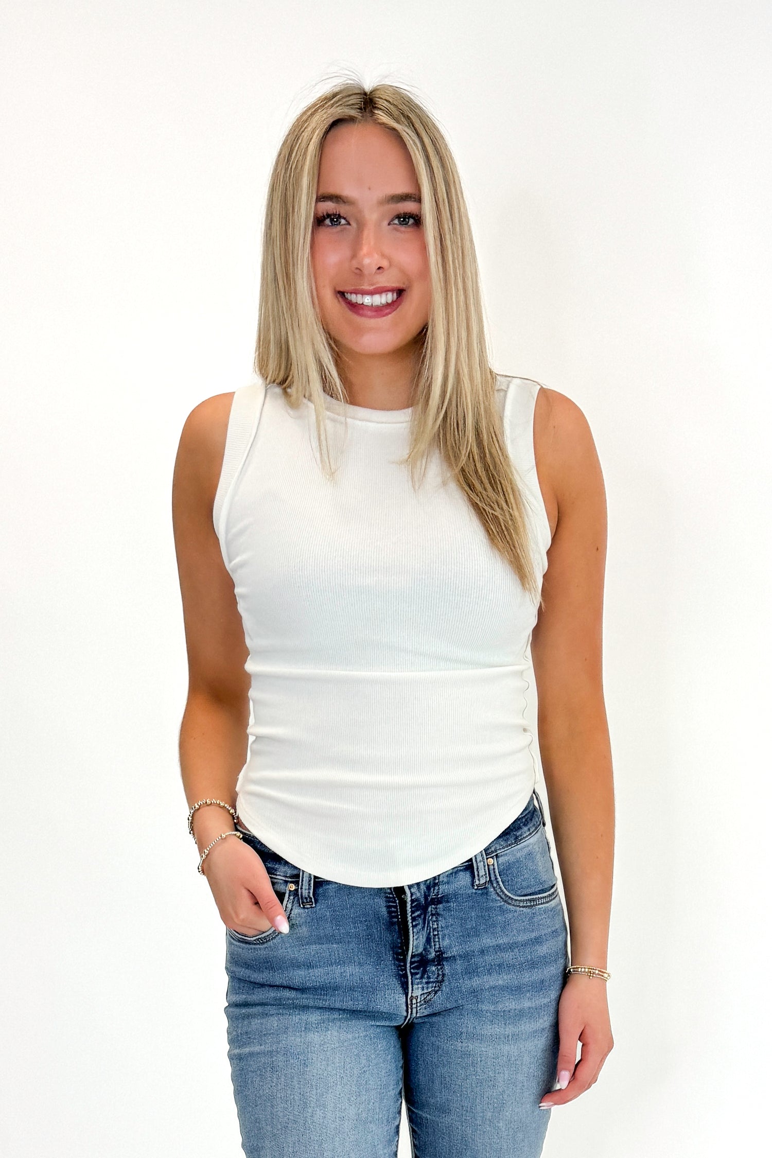 Front view of woman wearing Swagger  Off White Round Hem Ribbed Tank with jeans against white studio background.