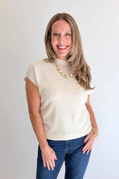 Front view of woman wearing Swagger Boutique’s Off White Shirred Cap Sleeve Sweater with jeans against white studio background.