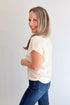 Side view of woman wearing Swagger Boutique’s Off White Shirred Cap Sleeve Sweater with jeans against white studio background.