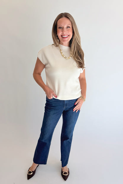 Front view of woman wearing Swagger Boutique’s Off White Shirred Cap Sleeve Sweater with jeans against white studio background.