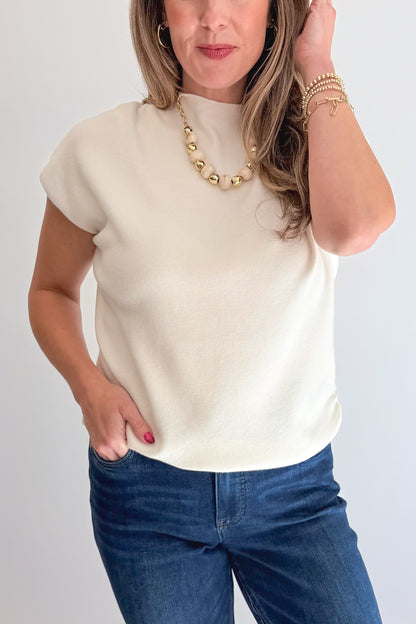 Front detail view of woman wearing Swagger Boutique’s Off White Shirred Cap Sleeve Sweater with jeans against white studio background.