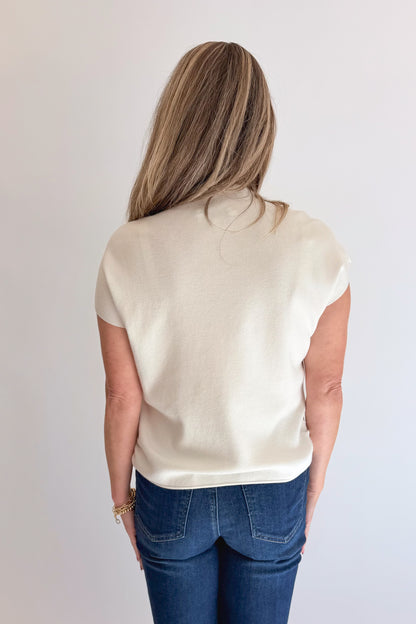 Back view of woman wearing Swagger Boutique’s Off White Shirred Cap Sleeve Sweater with jeans against white studio background.