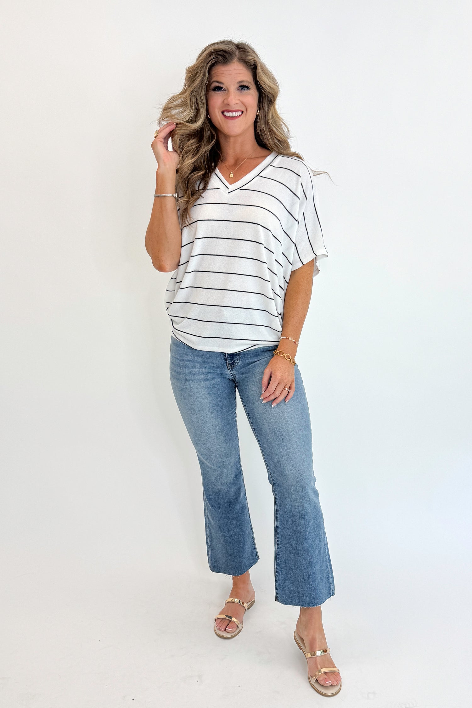 Front view of woman wearing Swagger Boutique’s Off White Striped Cocoon Top with jeans against white studio background.