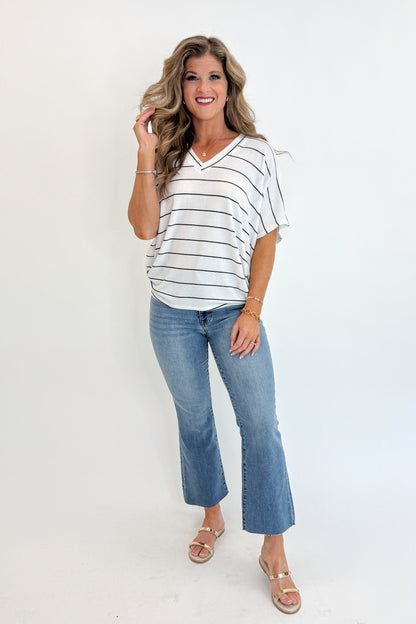 Front view of woman wearing Swagger Boutique’s Off White Striped Cocoon Top with jeans against white studio background.