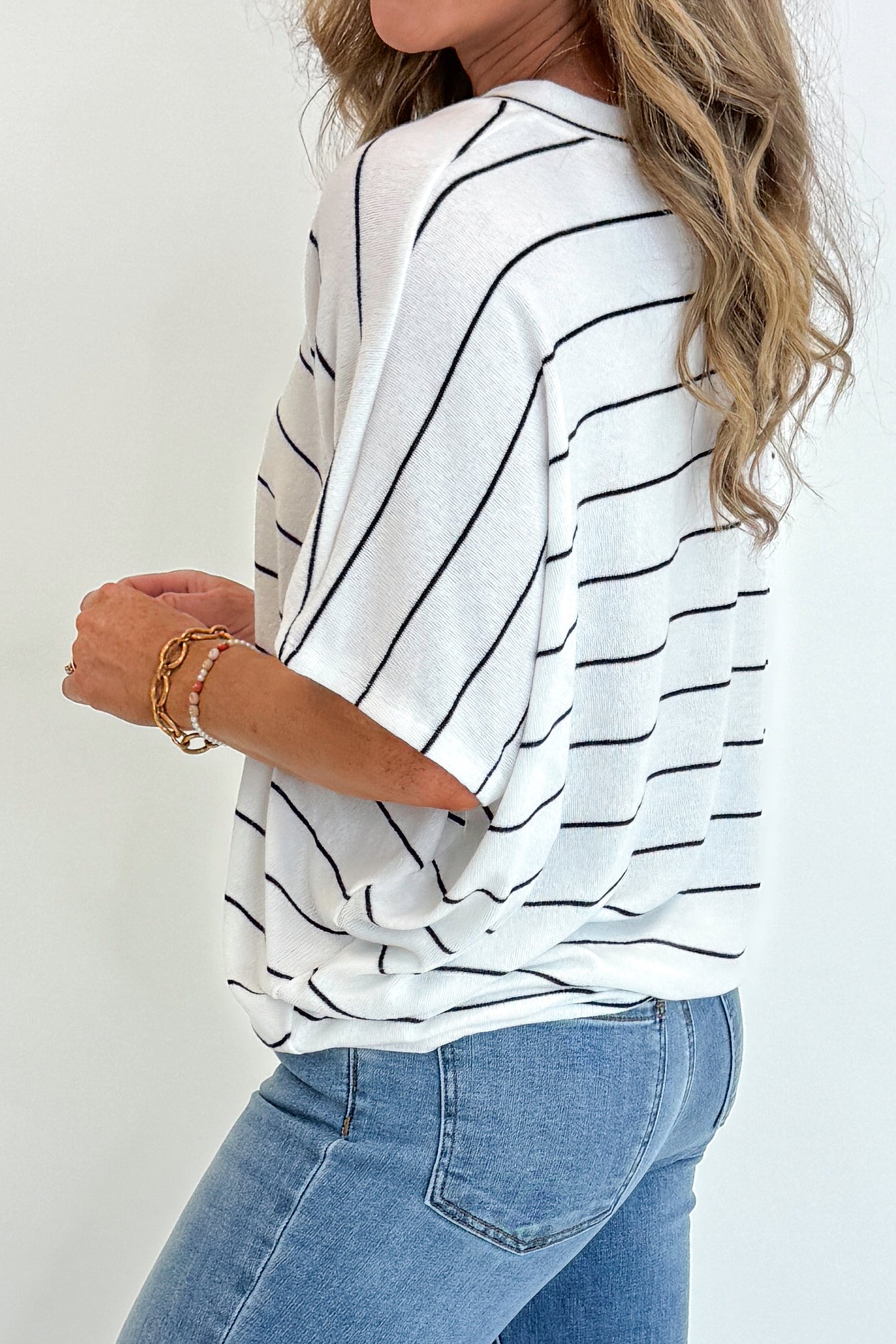 Side detail view of woman wearing Swagger Boutique’s Off White Striped Cocoon Top with jeans against white studio background.