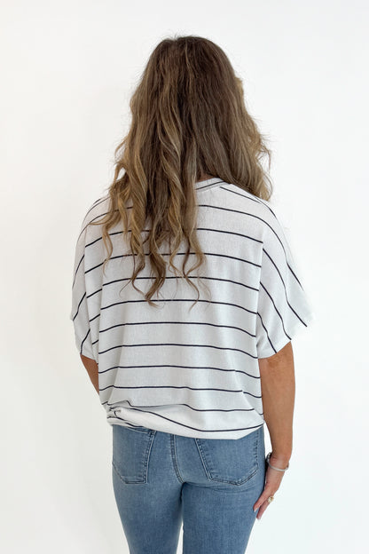 Back view of woman wearing Swagger Boutique’s Off White Striped Cocoon Top with jeans against white studio background.