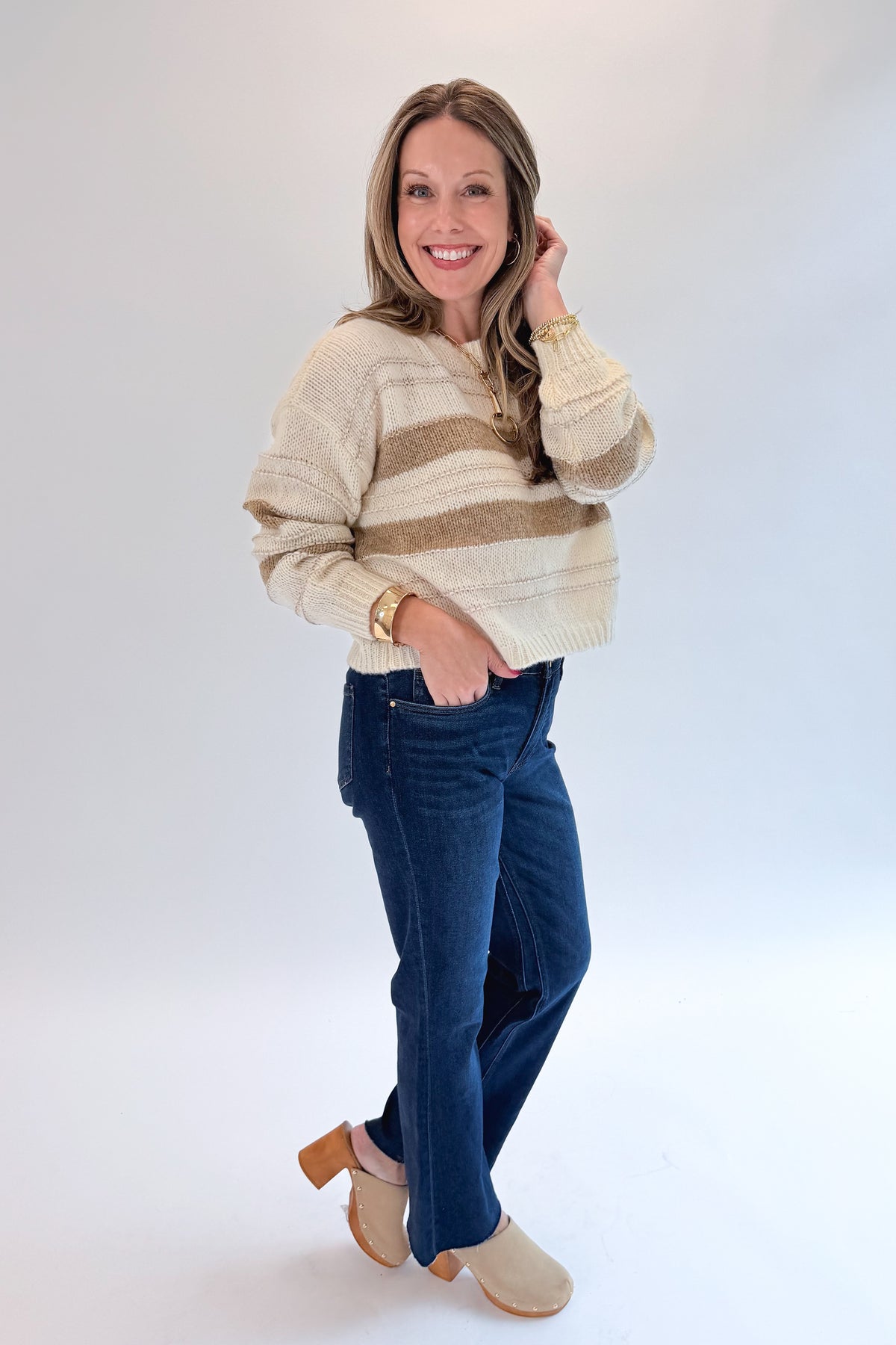 Side view of woman wearing Swagger Boutique’s Off White, Beige and Metallic Stripe Sweater by Molly Bracken with jeans against white studio background.