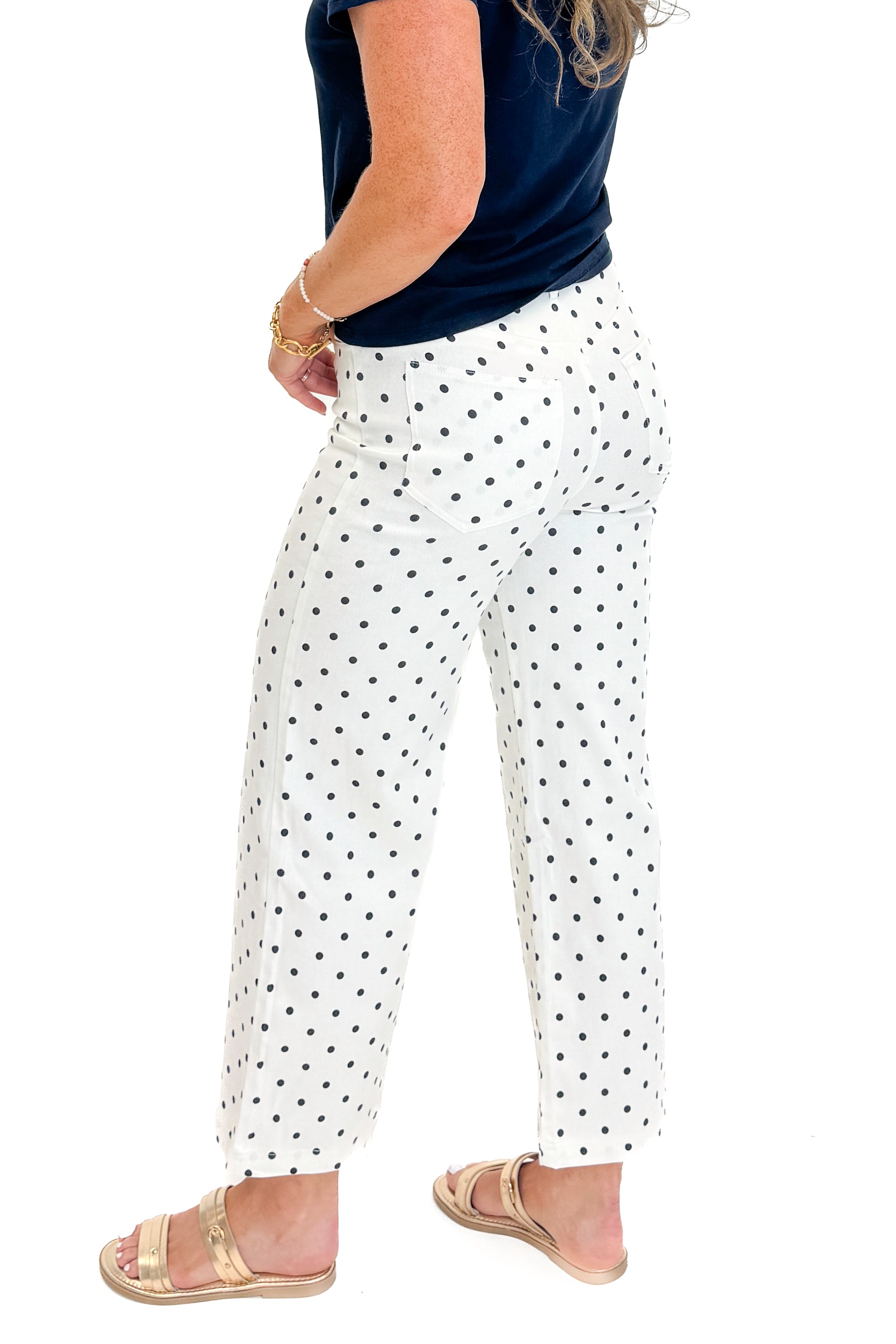 Side view of woman wearing Swagger Boutique’s Off White &amp; Navy Polka Dot Jeans by Entro with navy top against white studio background.