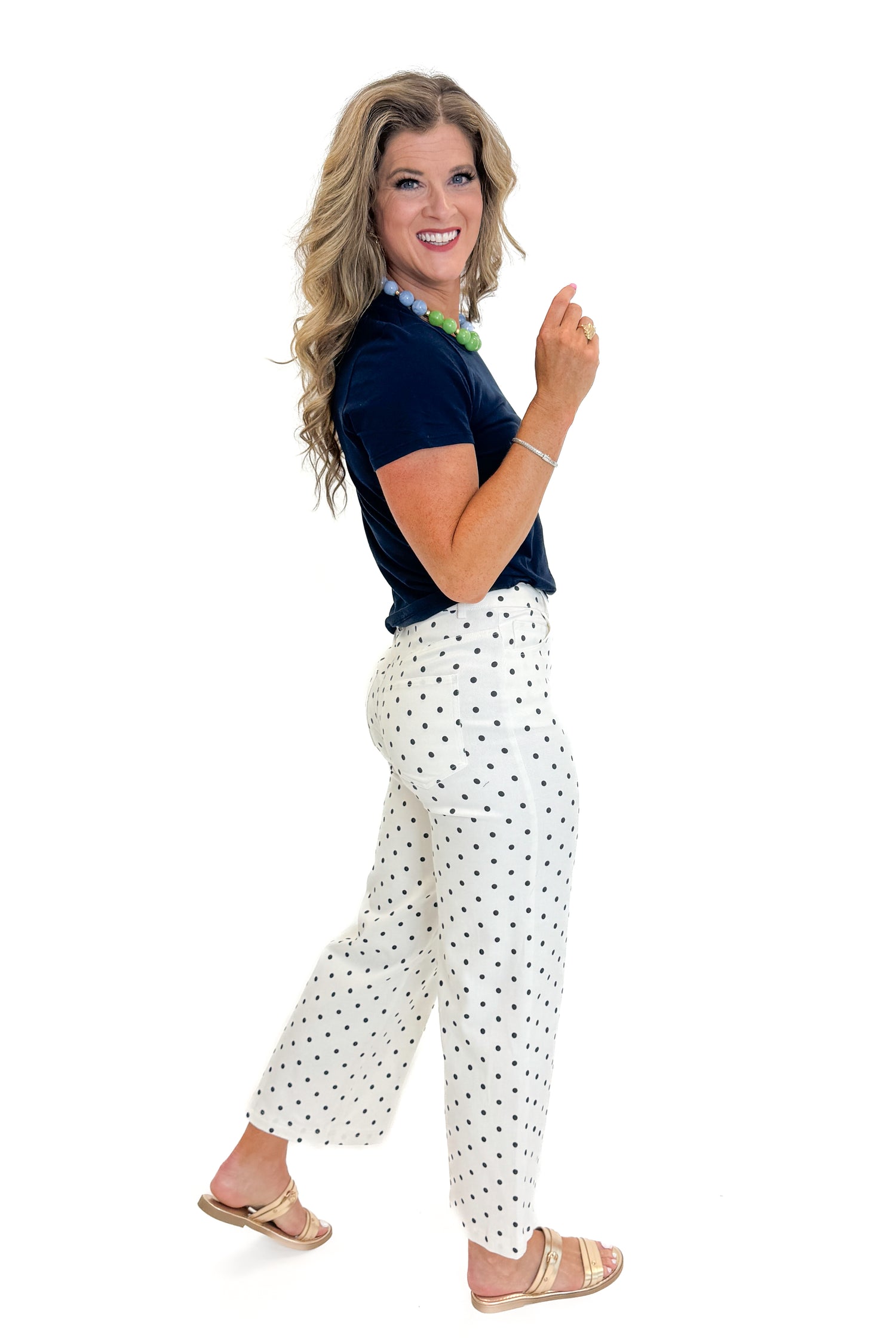Side view of woman wearing Swagger Boutique’s Off White &amp; Navy Polka Dot Jeans by Entro with navy top against white studio background.
