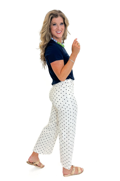 Side view of woman wearing Swagger Boutique’s Off White &amp; Navy Polka Dot Jeans by Entro with navy top against white studio background.