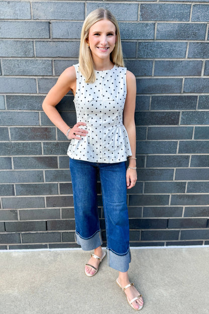 Front view of woman wearing Swagger Boutique’s Off White &amp; Navy Polka Dot Peplum Tank by Entro with Jeans standing outside.