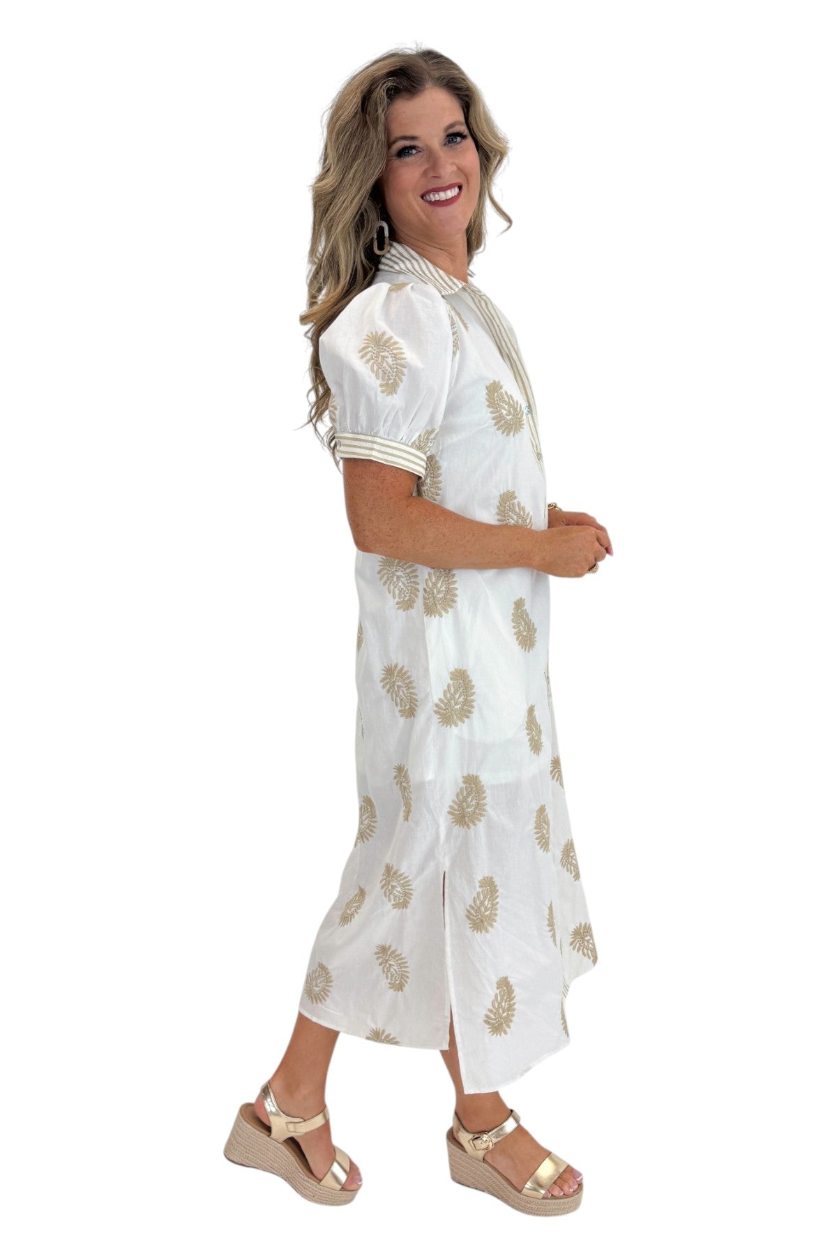 Side view of woman wearing Swagger Boutique’s Off White &amp; Taupe Embroidered Midi Dress with sandals against white studio background.