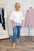 Front view of woman wearing Swagger Boutique’s Off White Asymmetrical Lace Hem Top by Entro with jeans against white studio background.