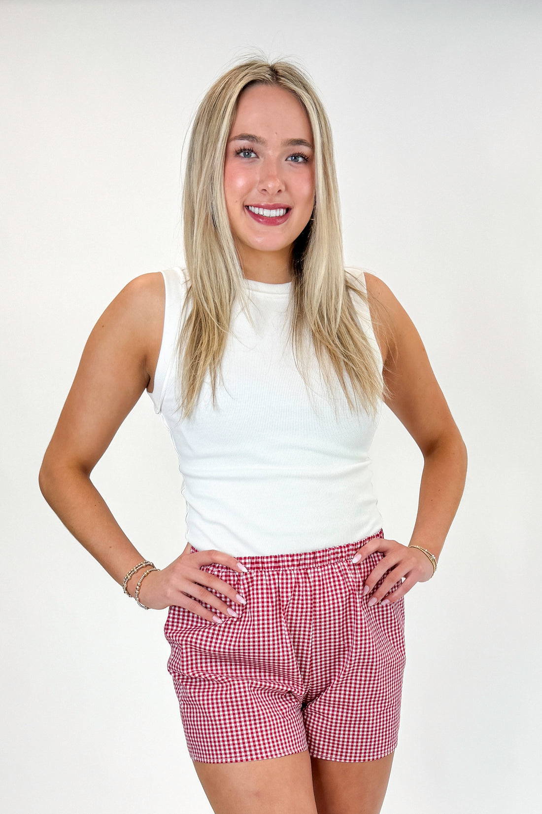 Front view of woman wearing Swagger Boutique’s Red Gingham Shorts with Off White Round Hem Ribbed Tank against white studio background.