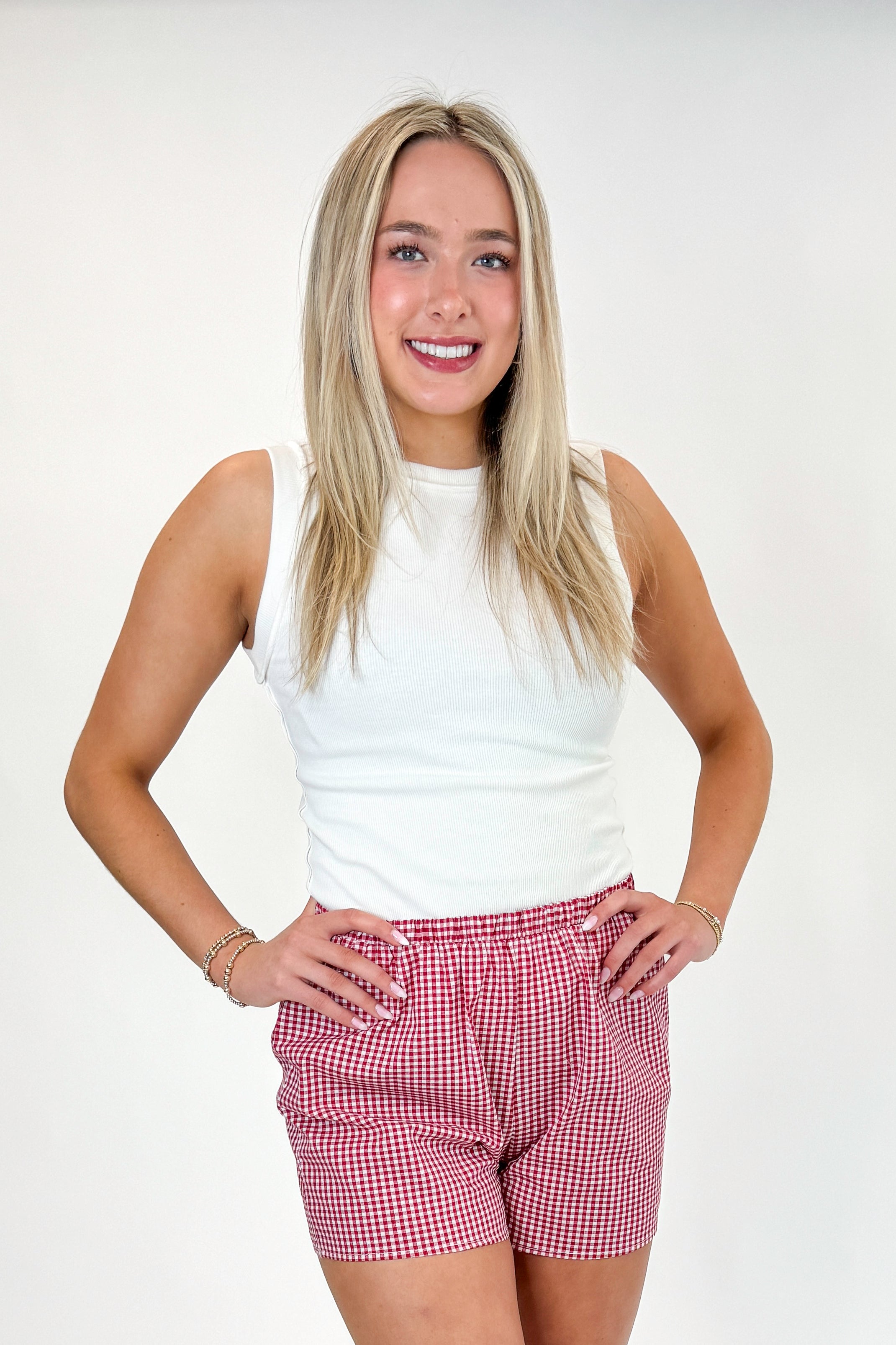 Front view of woman wearing Swagger Boutique’s Red Gingham Shorts with Off White Round Hem Ribbed Tank against white studio background.