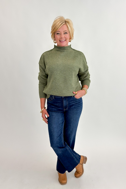 Front view of woman wearing Swagger Boutique’s Olive Mock Neck Sweater by Entro with jeans against white studio background.