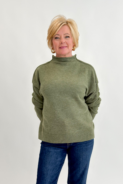 Front view of woman wearing Swagger Boutique’s Olive Mock Neck Sweater by Entro with jeans against white studio background.