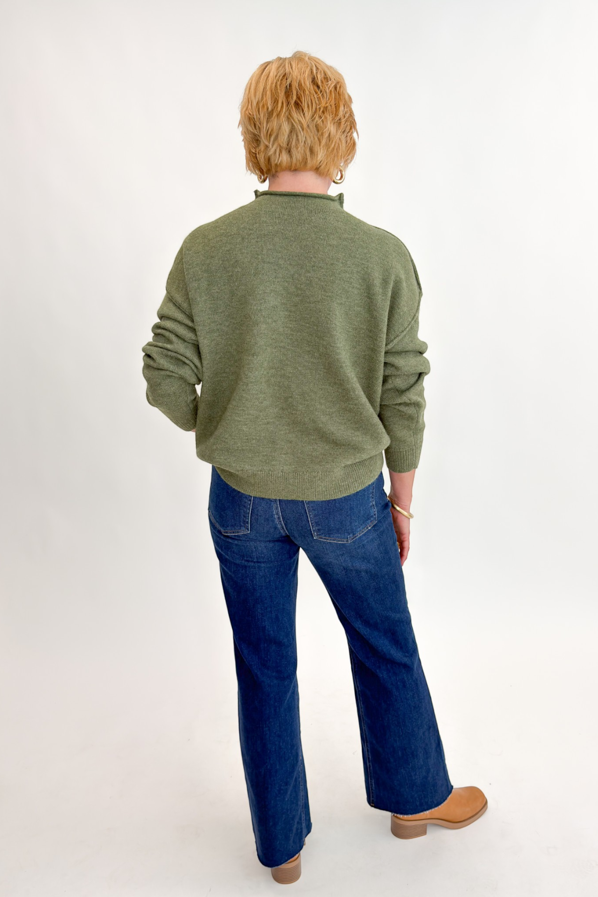 Back view of woman wearing Swagger Boutique’s Olive Mock Neck Sweater by Entro with jeans against white studio background.