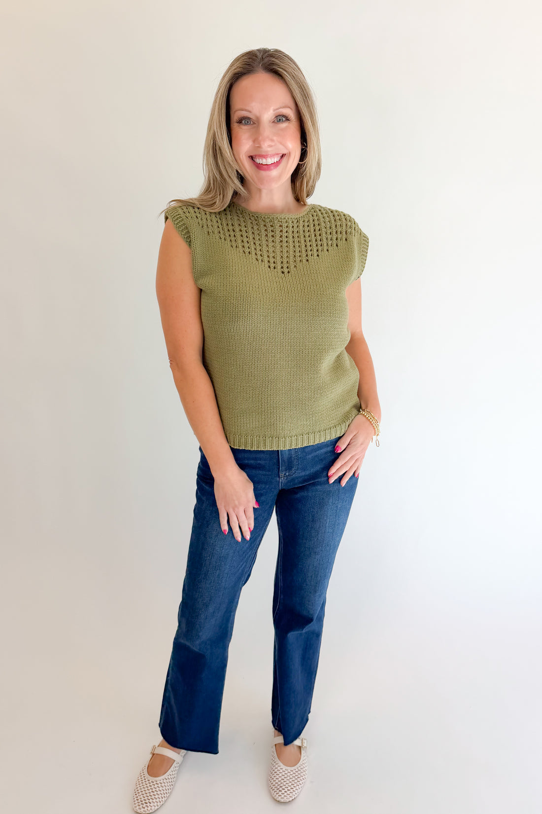 Front view of woman wearing Swagger Boutique’s Olive Open Knit Sleeveless Sweater with jeans against white studio background.