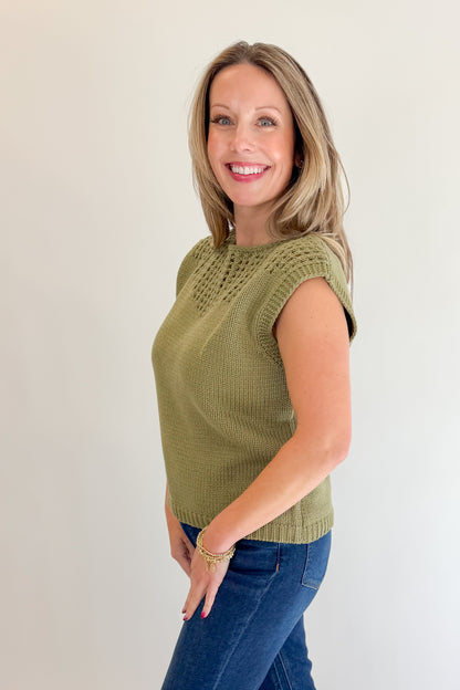 Side view of woman wearing Swagger Boutique’s Olive Open Knit Sleeveless Sweater with jeans against white studio background.
