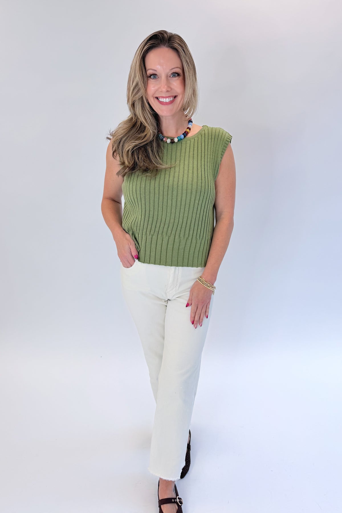 Front view of woman wearing Swagger Boutique’s Olive Ribbed Sleeveless Sweater with jeans against white studio background.