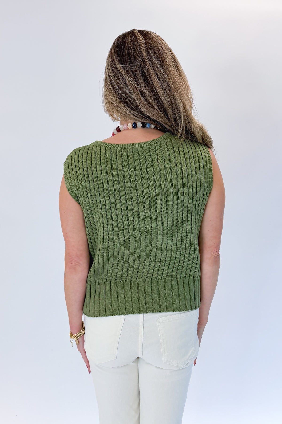 Back view of woman wearing Swagger Boutique’s Olive Ribbed Sleeveless Sweater with jeans against white studio background.