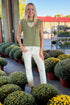 Front view of woman wearing Swagger Boutique’s Olive Ribbed Sleeveless Sweater with jeans at a garden center.
