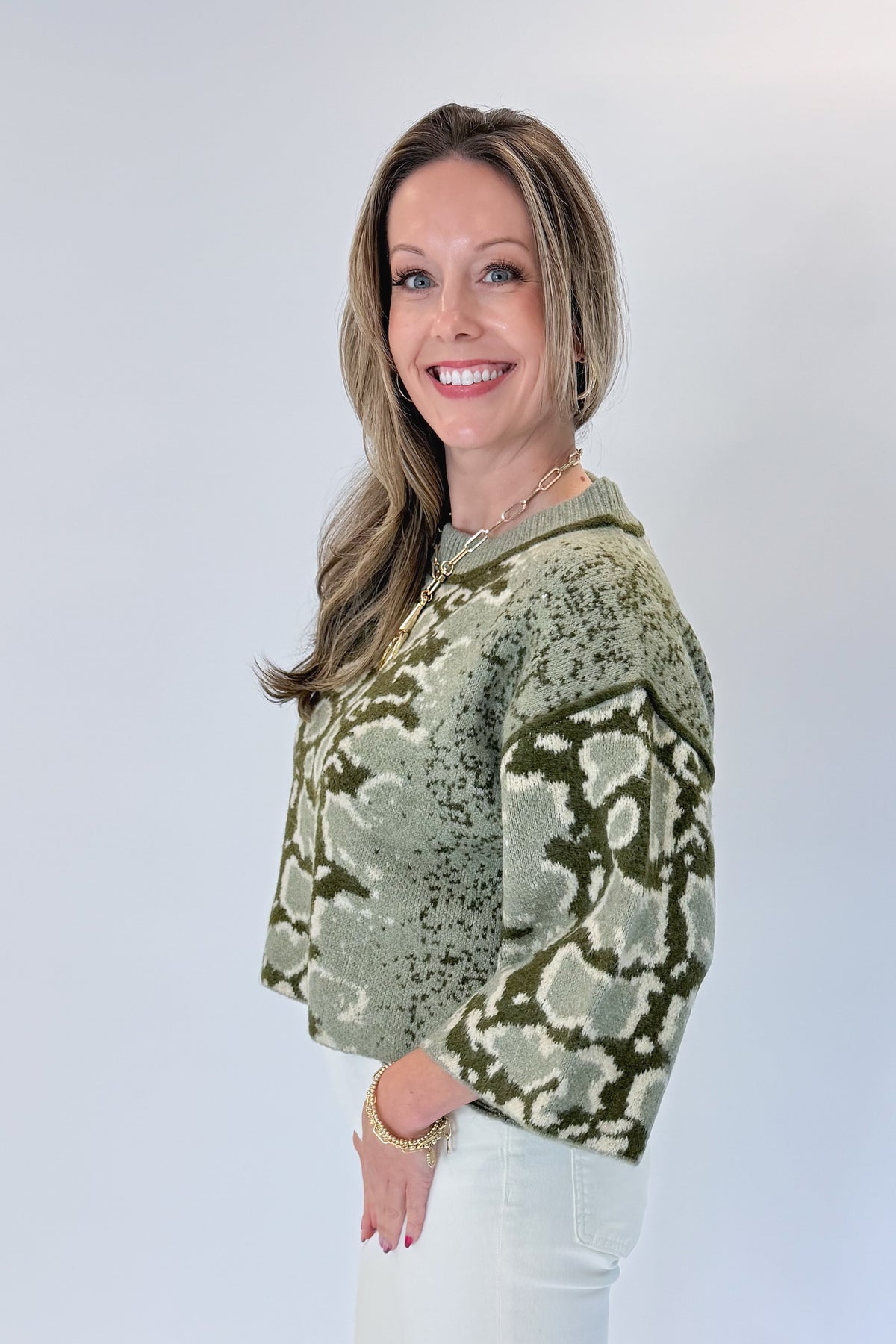 Side view of woman wearing Swagger Boutique’s Olive Snake Print Sweater by Entro with jeans against white studio background.