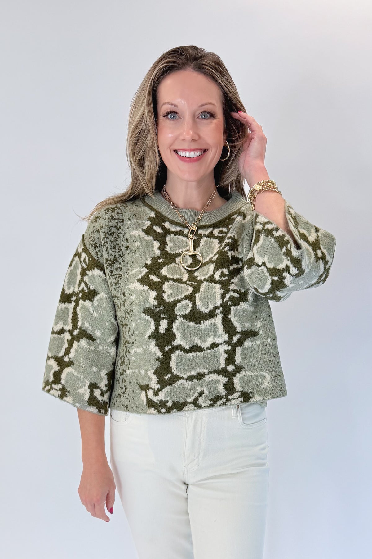 Front view of woman wearing Swagger Boutique’s Olive Snake Print Sweater by Entro with jeans against white studio background.