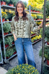 Front view of woman wearing Swagger Boutique’s Olive Snake Print Sweater by Entro with jeans at a garden center.