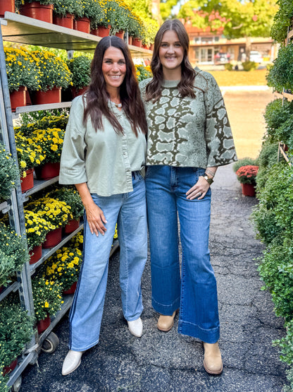 Front view of women wearing Swagger Boutique’s Olive Snake Print Sweater by Entro and Washed Olive 3/4 Sleeve Button Down Top with jeans at a garden center.