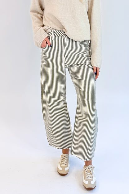 Front detail view of woman wearing Swagger Boutique’s top with Olive Striped Barrel Jeans by Just Black Denim against white studio background.